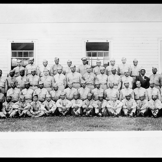 Grey Scale photo of men in uniform lined up infront of a wall standing in 4 rows