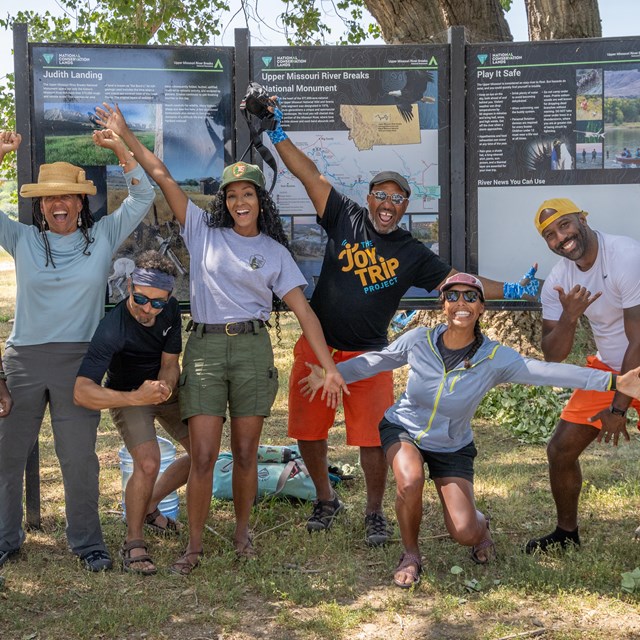 Eight people cheerily posing in front of a visitor sign at Judith Landing