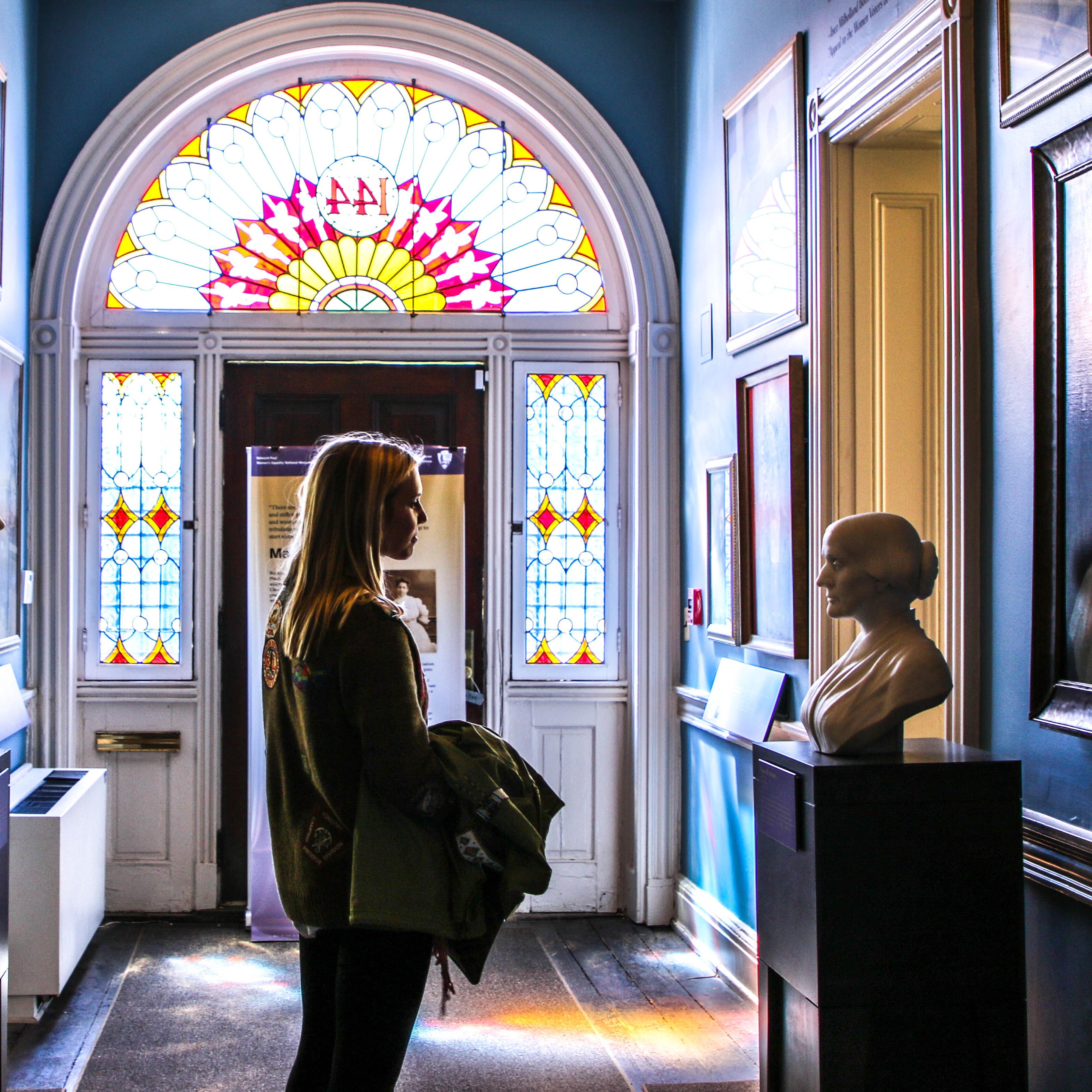 Visitor in a hallway of suffragist busts and paintings