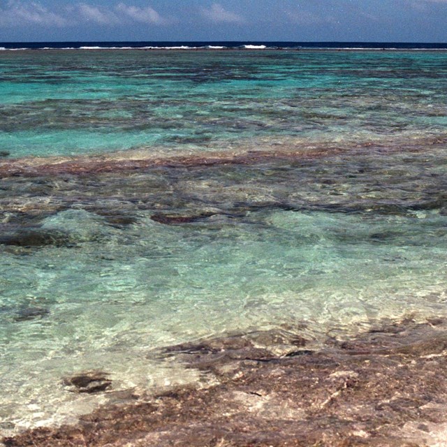 An overhead view of a lagoon with shallow, clear water with some coral reefs visible.