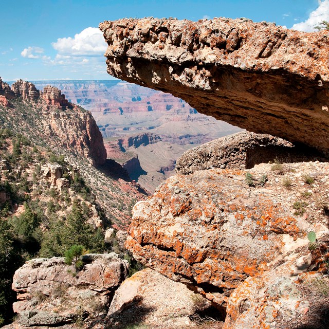 Photo of layered rock with cliffs and canyons in the distance.