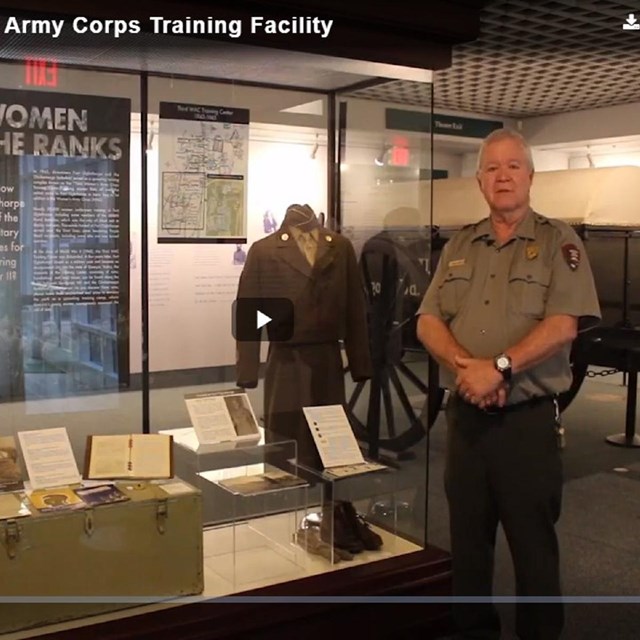 A video still of an older white man in park ranger uniform standing next to museum display