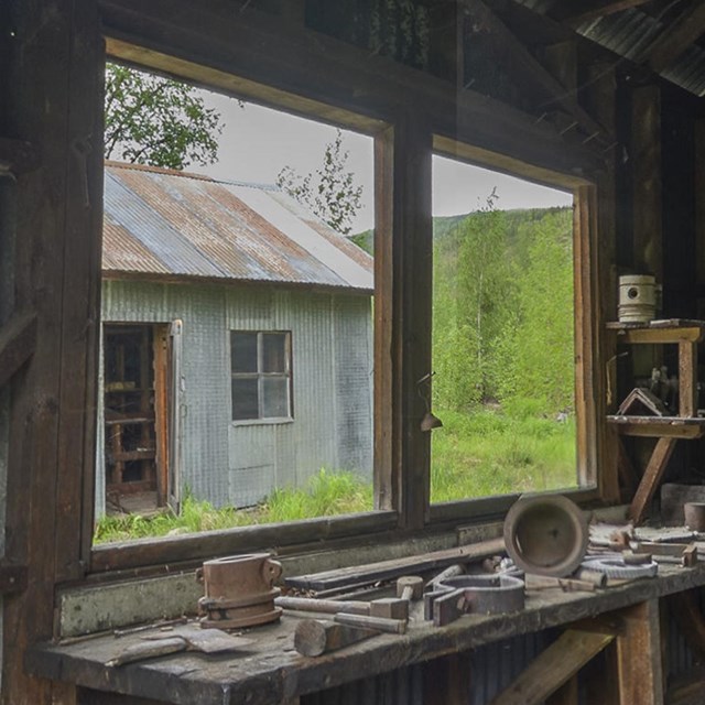 Photograph of table with blacksmith tools and window with green trees and shed