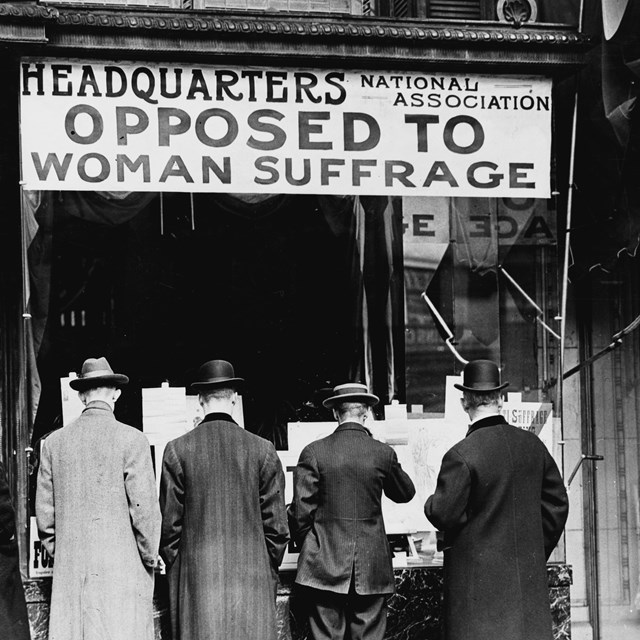 Men looking in window of headquarters opposed to woman suffrage