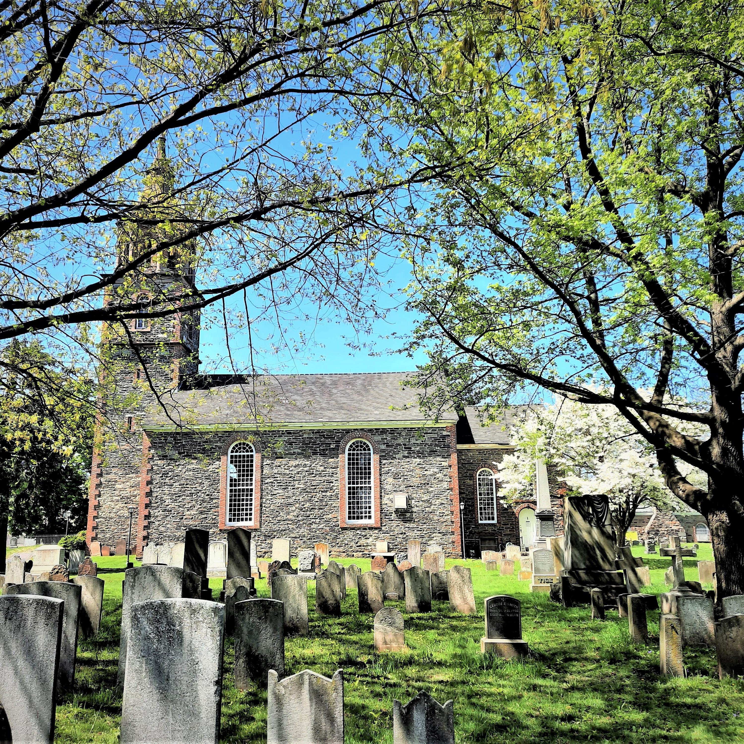 A stone church surrounded by trees with a graveyard in the foreground
