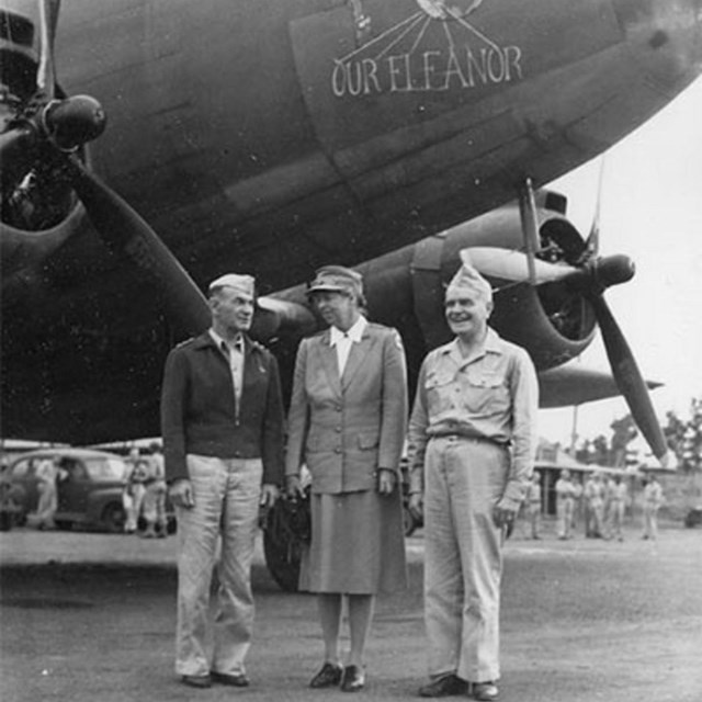 Two men and a woman stand on an airport tarmac in front of a large plane with text 