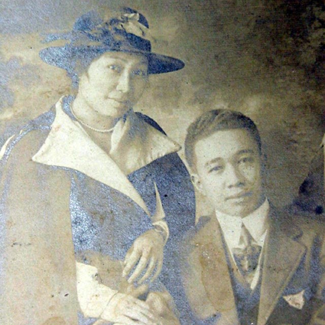 A young woman in hat and coat leans against a young man in suit
