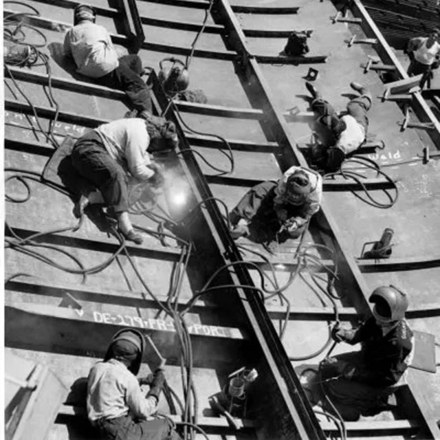 Women in masks work welding on the side of a ship