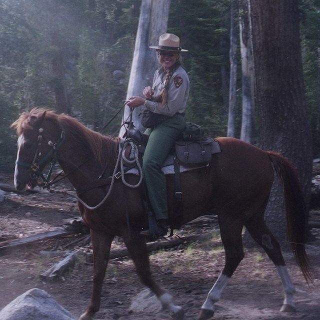 White woman with blonde hair wearing NPS uniform and riding horse