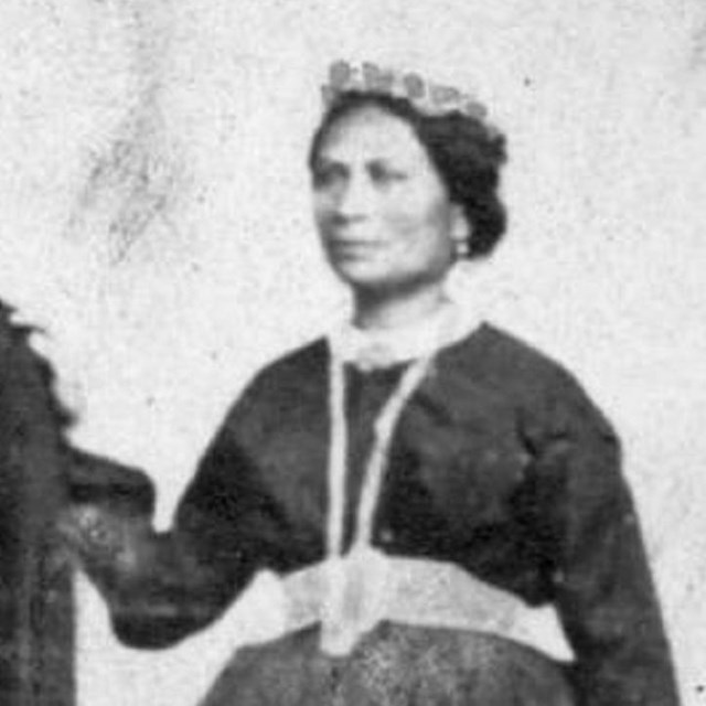 A black and white photograph of a Hawaiian woman wearing a dark dress with a white collar.
