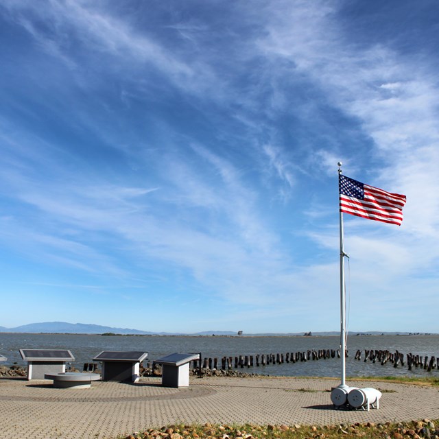 American flag and four plaques next to a set of pilings in the water.