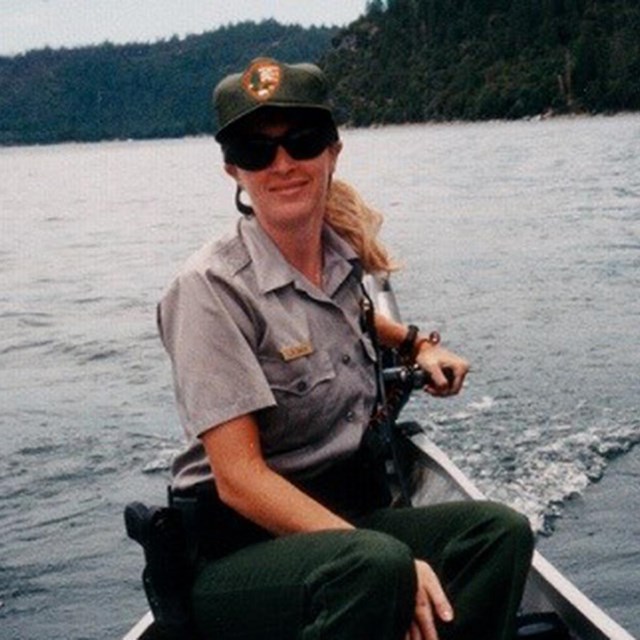 Leslie steers a boat on a lake with mountains in the background