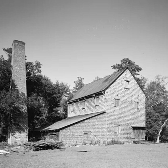 Greyscale photo of a farmhouse in front of a large group of trees