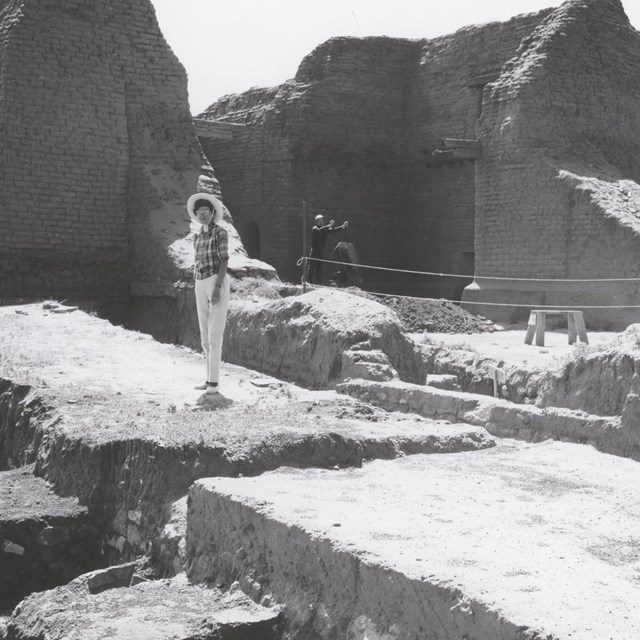 Archeologist Jean Pinkley standing on top of the ruins at Pecos, wearing a plaid shirt and a hat.