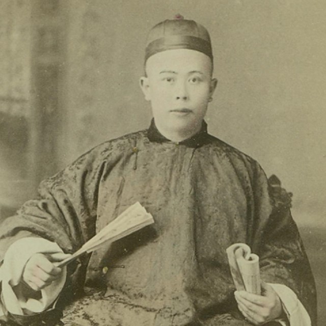 A Chinese man in traditional clothing poses for a black and white photo.