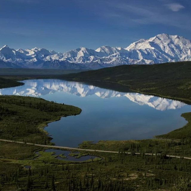 Aerial view of a reflective lake with snowy mountains in the background.