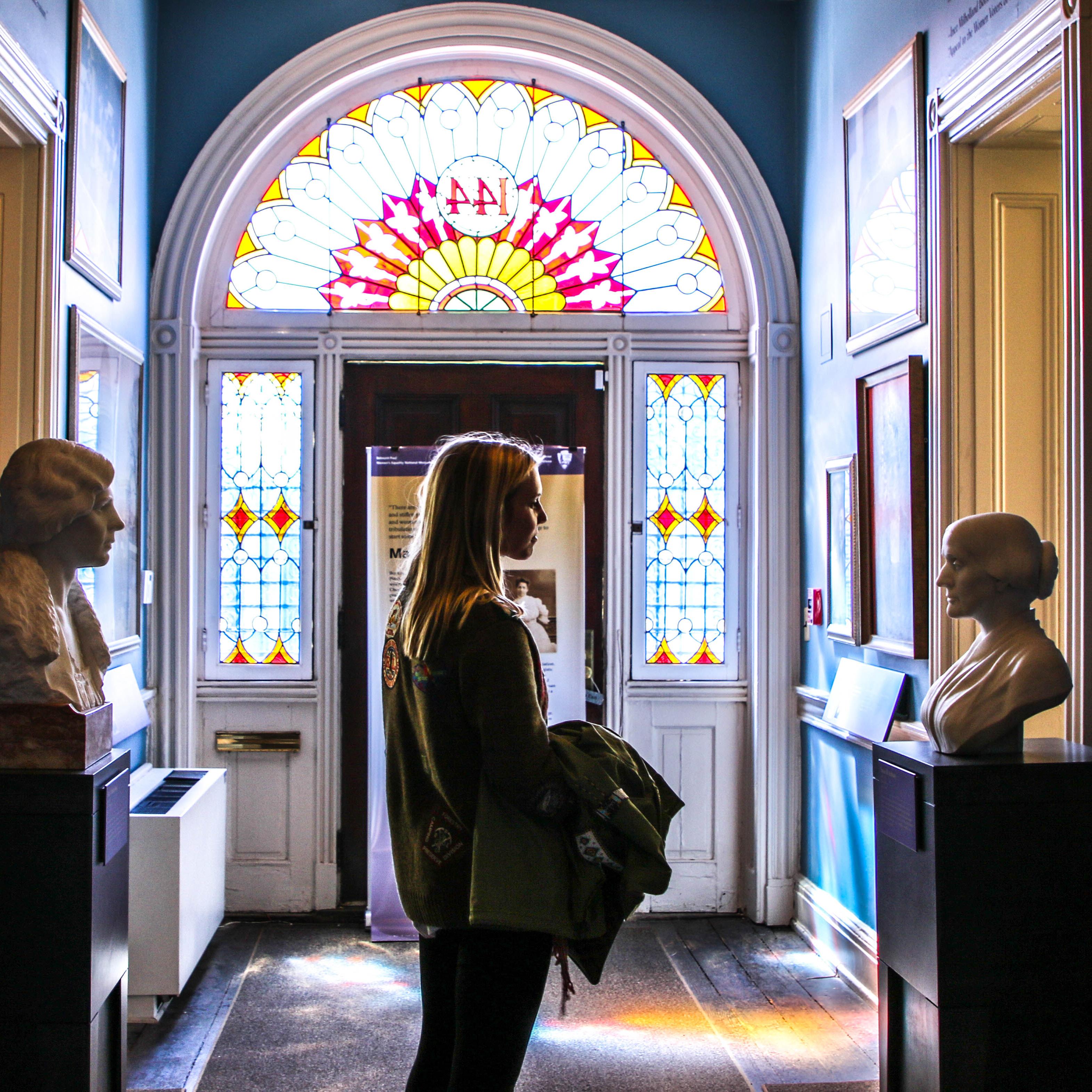 White woman standing in a hallway looking at a bust and painting