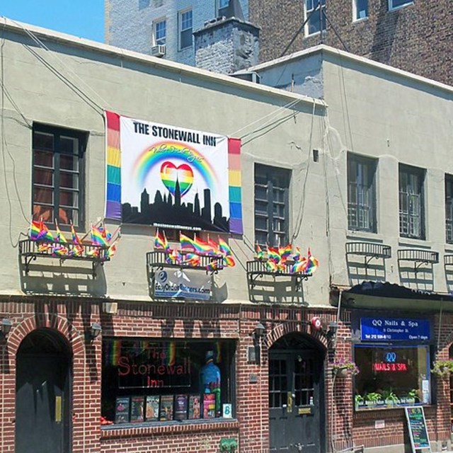 Color photograph of the exterior of the Stonewall Inn. Rainbow flags decorate the building.