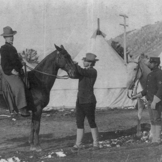 (U.S. soldier-guide holding woman's horse, African American trooper alongside, tents in background, 
