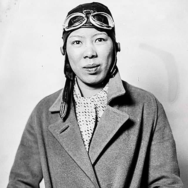Black and white photo of a Chinese American woman wearing aviator's goggles and cap.