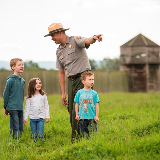 A park ranger standing in front of Fort Vancouver with a group of kids.