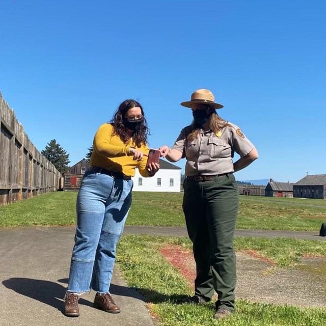 A park ranger and a visitor looking at a cell phone inside Fort Vancouver.