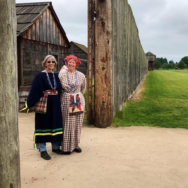 Two volunteers in period costumes stand at the entrance to Fort Vancouver.