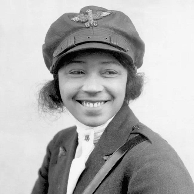 Black woman smiles at camera with a pilots cap on