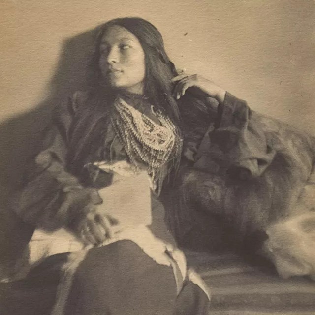 Woman with long dark hair lounges in front of camera while looking off to the side.