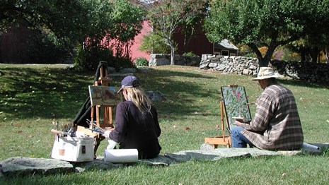 two people sitting on a lawn, painting
