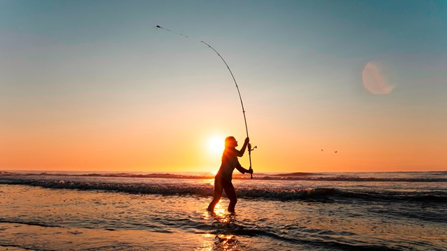 Visitor casting surf fishing rod at the ocean's edge