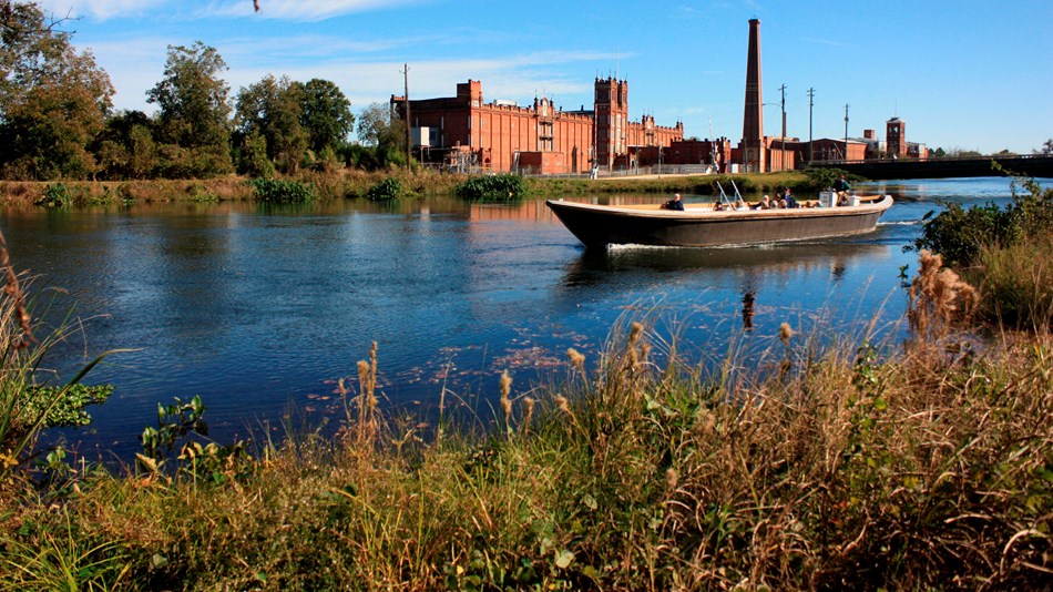 Boat traveling down canal with mill in background