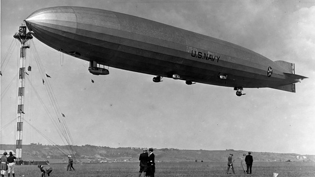 A large blimp air ship docked to a tall tower