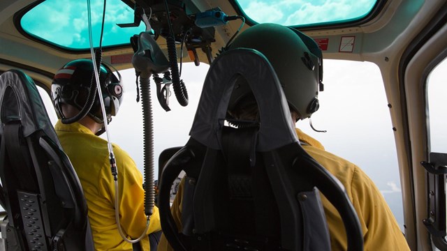 A pilot and co-pilot fly in an aircraft above an obscured landscape.