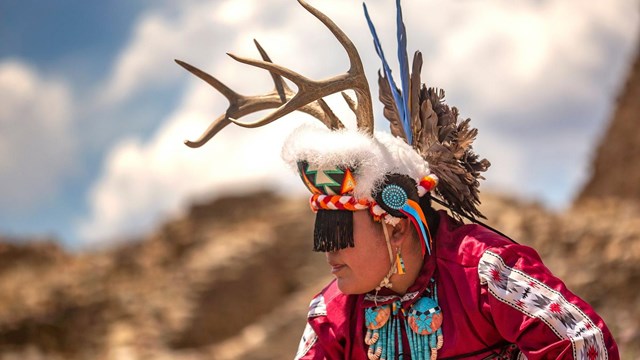 A Pueblo dancer wearing traditional regalia and antlers dancing in the Aztec West plaza.