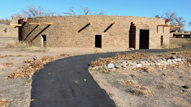 A paved path leading up to the Aztec West Great Kiva under a blue sky.
