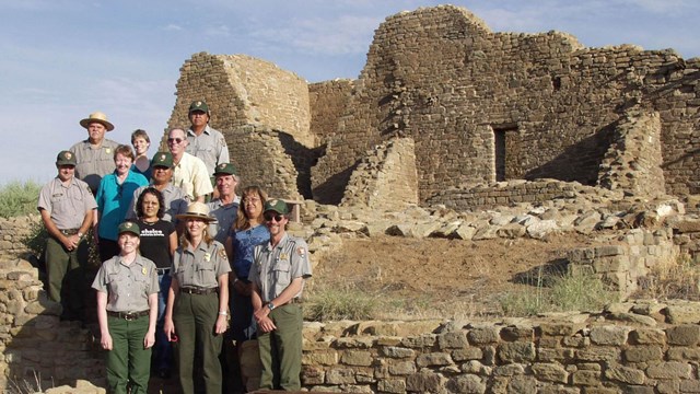 A group of rangers in and out of uniform standing in front of ancient ruins.