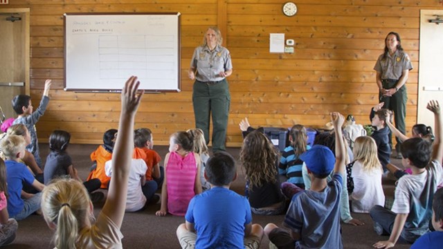 A ranger standing at the front of a room giving an education program to a group of students.