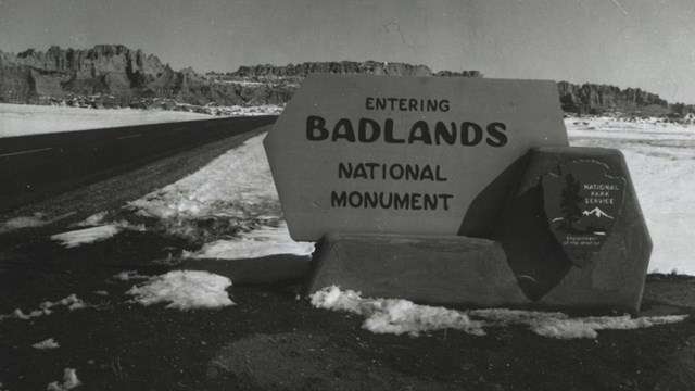a historic black and white photo of the original park sign: "entering badlands national monument"