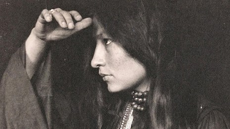 Black and white portrait of an American Indian woman with her hand up to her face.