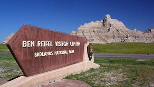 Picture of the Ben Reifel Visitor Center Sign with Badlands Formation in the Background.