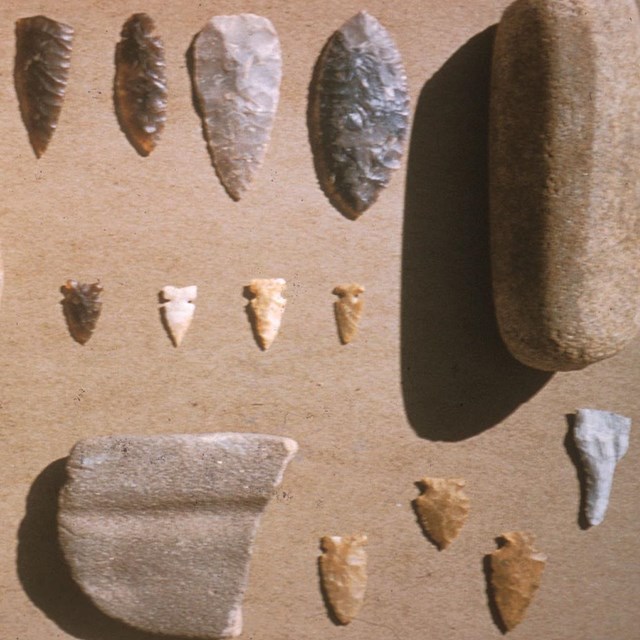 various worked stones such as arrowheads in a wide range of sizes lay on a brown cloth