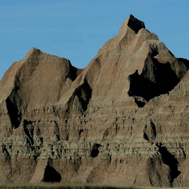 a large jagged butte with various layers reaches into a clear blue sky