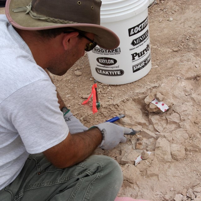 a man works at chipping away hard sandstone using a variety of tools like hammers.