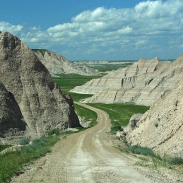 a dirt road winds through a low point between buttes and disappear into a grassy valley.