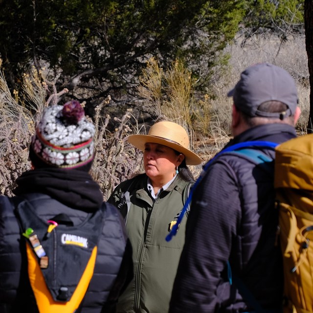 A female park ranger standing in front of visitors with backpacks and colorful jackets.