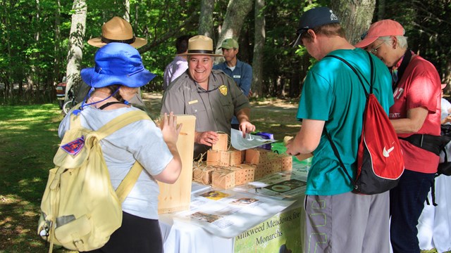 group of people stand around an outdoor table covered with bat houses