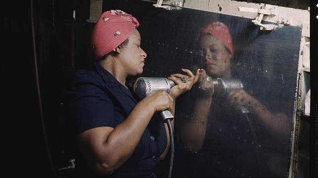 Black woman in red bandanna operates power drill on plane