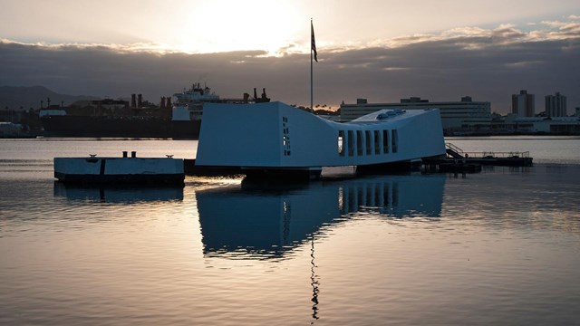 White memorial building appears suspended over water at Pearl Harbor at sunset