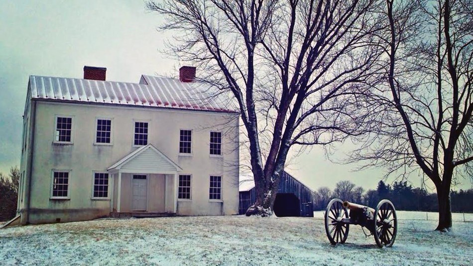 Simple two-story white house stands in snowy field with cannon